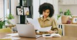Young woman going through paperwork while working on a laptop at home.
