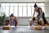 Young asian male yoga instructor guiding two young female adults on yoga stretching.