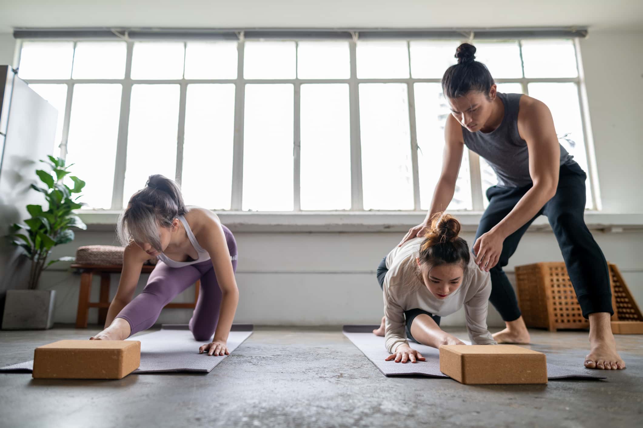 Young asian male yoga instructor guiding two young female adults on yoga stretching.