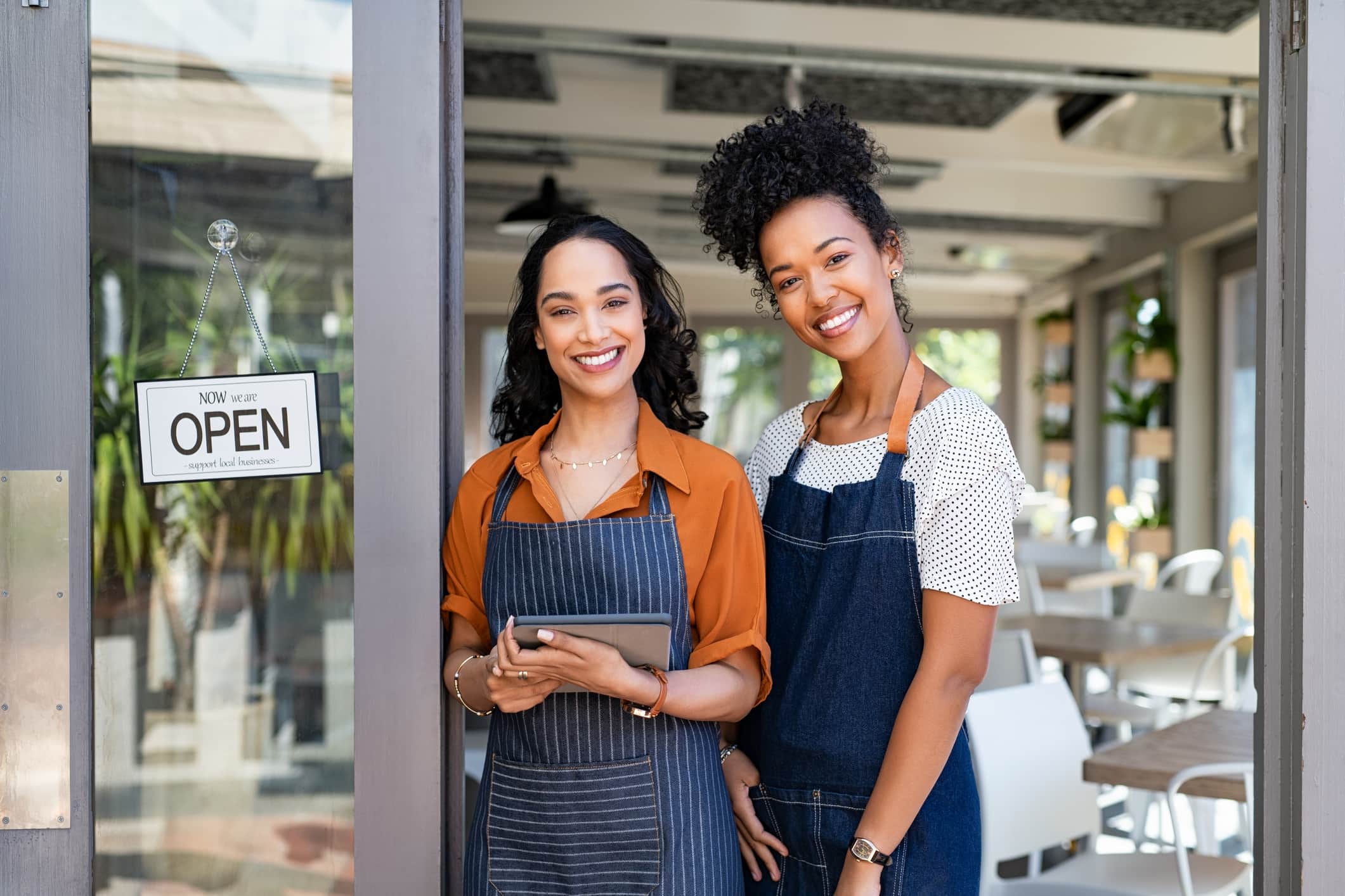 Two successful female waitress standing at a cafe entrance door.