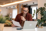 Small business owner researching insurance on computer at home.