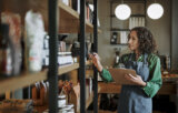 Deli owner taking inventory on store shelves using a clipboard