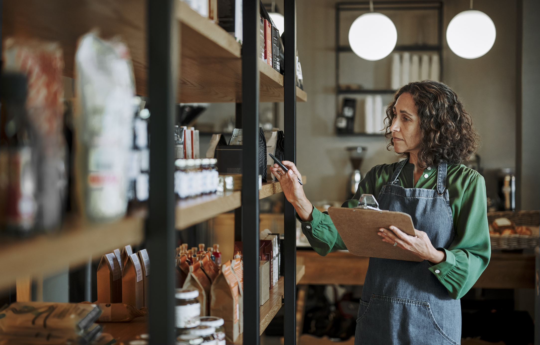Deli owner taking inventory on store shelves using a clipboard